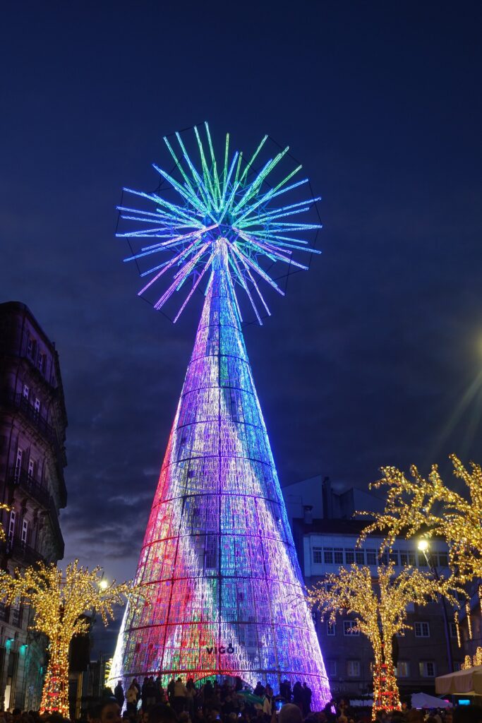 El árbol gigante de Navidad de la Porta do Sol de Vigo con patrones lumínicos multicolor, de noche, rodeado de árboles iluminados y con público a sus pies